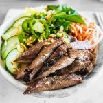A close-up of a delicious beef salad bowl featuring fresh cucumbers, herbs, and chili peppers.