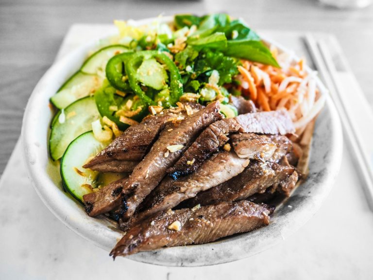 A close-up of a delicious beef salad bowl featuring fresh cucumbers, herbs, and chili peppers.
