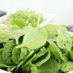 A close-up of fresh spinach leaves in a white bowl, ideal for healthy salads.